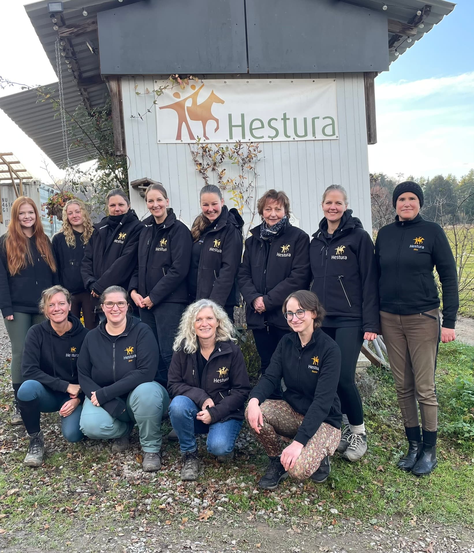 Das Hestura-Team in schwarzen Hestura-Jacken vor dem Hestura-Schild am Lindenhof