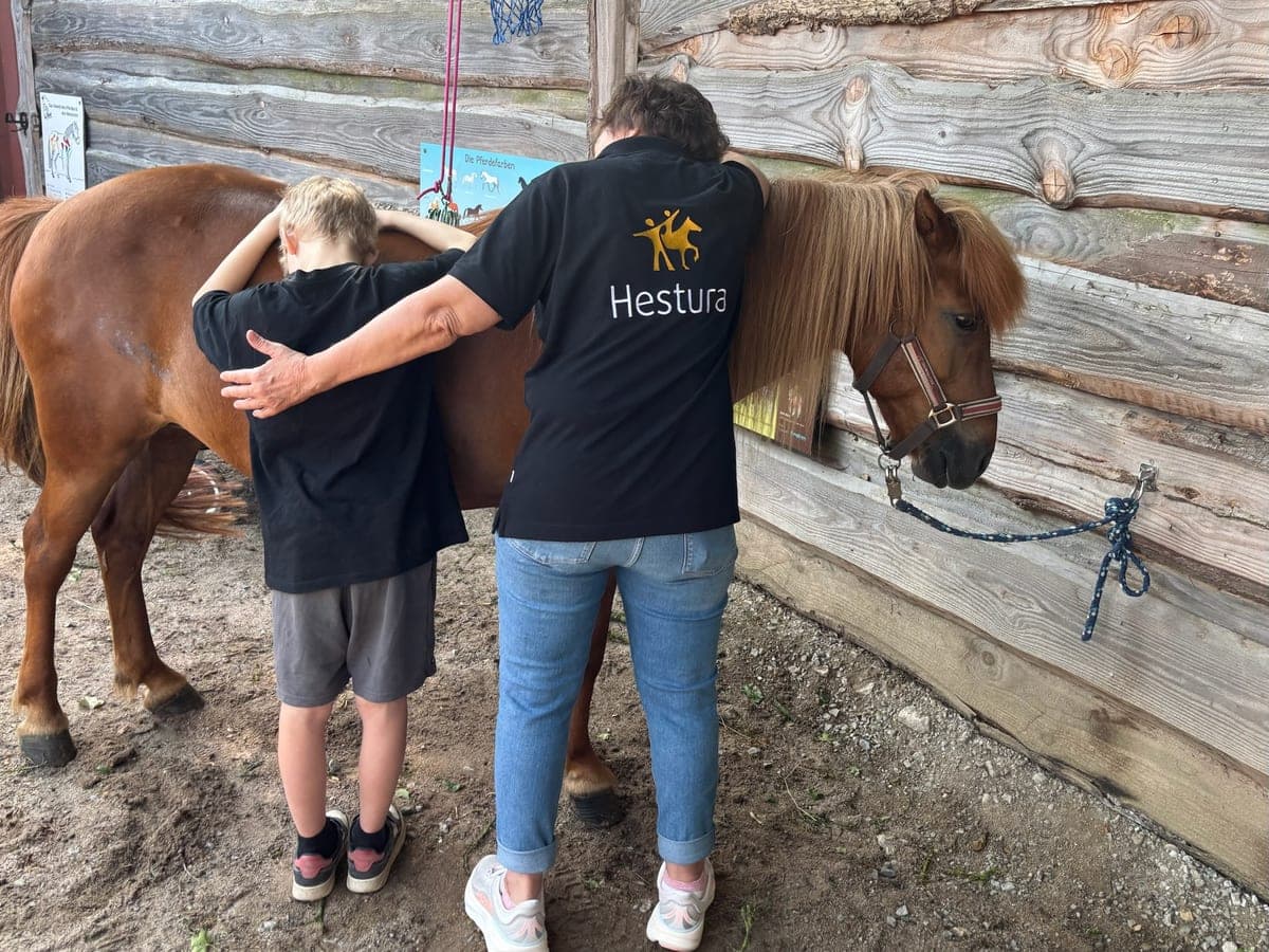 Eine Begleiterin legt den Arm um ein Kind, das neben einem Pony steht
