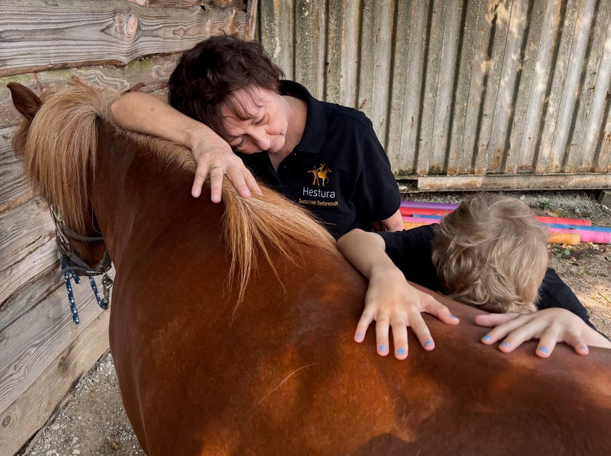 Susanne Behrendt lehnt sich an den Hals eines Ponys, daneben ein Kind